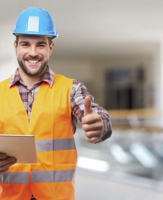 Smiling manual worker in blue helmet with digital tablet and gesture thumb up
